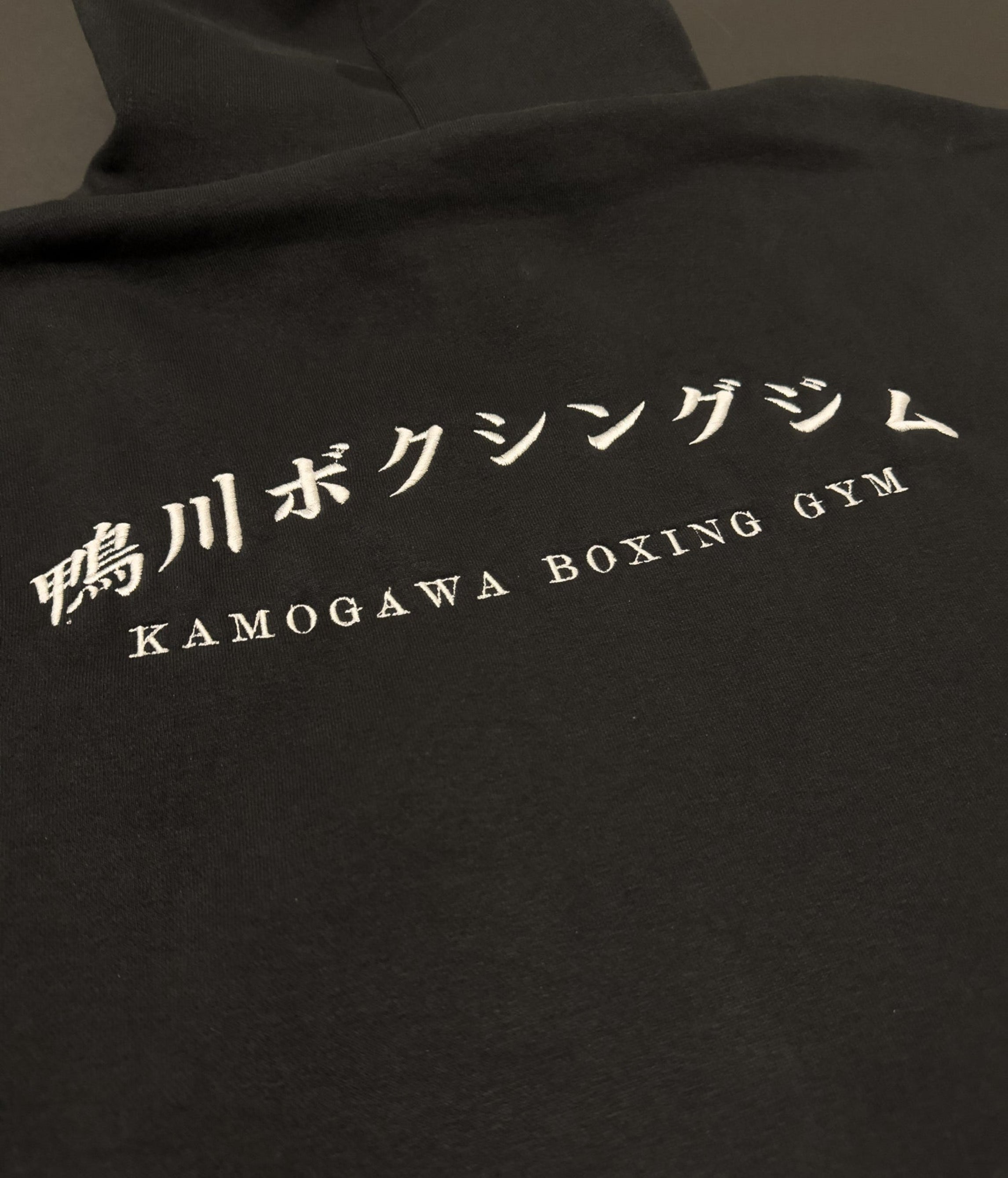 Black hoodie with 'Kamogawa Bokushingu Jimu' on the back