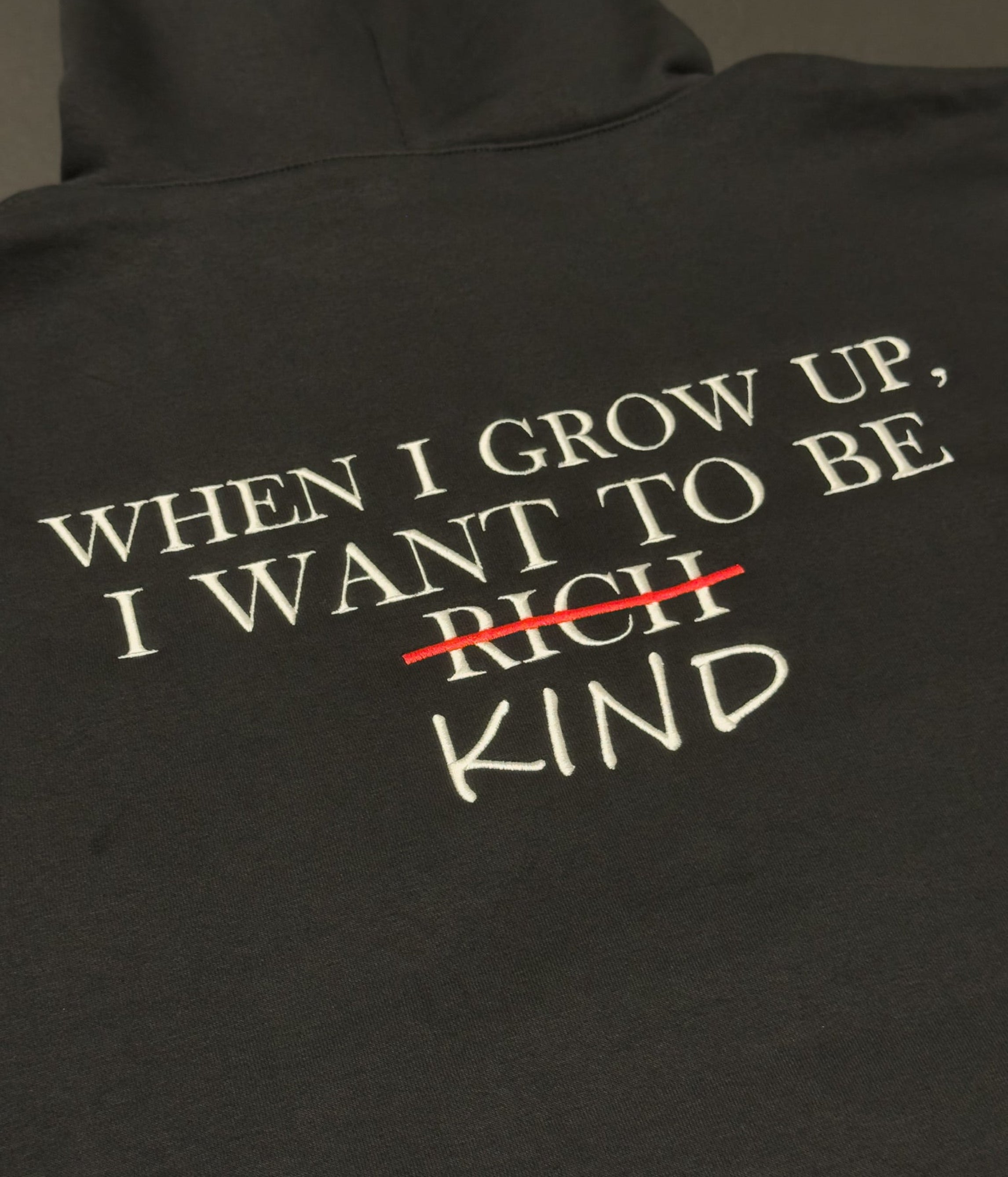 Black hoodie with embroidered text 'When I grow up I want to be rich kind' on the back