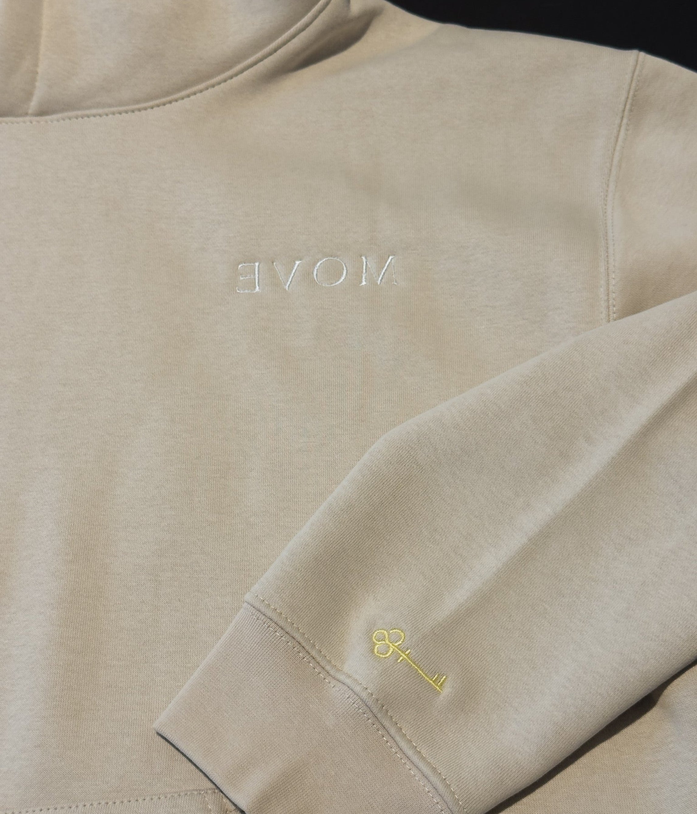 Bone hoodie with 'MOVE' text and key emblem on sleeve